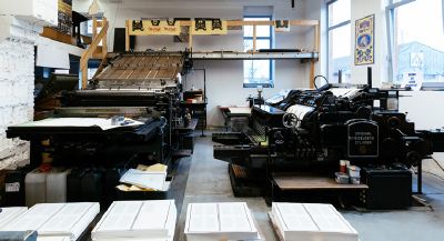 Die Suhrkamp Letterpress Druckmaschine in einer Werkstatt, im Vordergrund fertige Druckbögen.