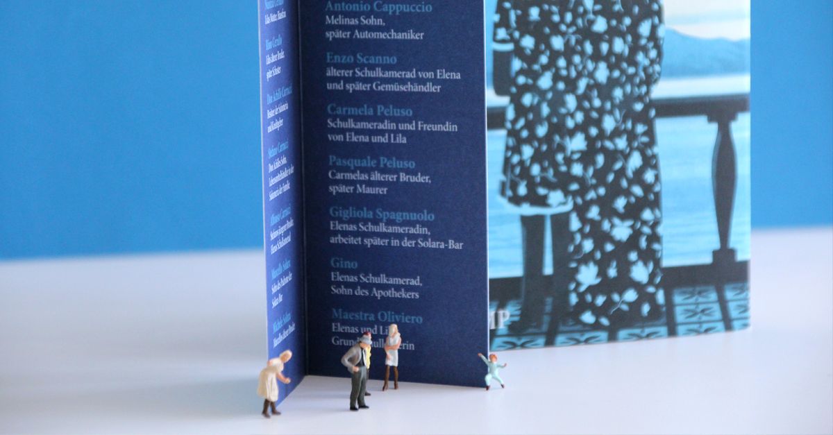 Vier Miniaturfiguren stehen vor einem aufgestellten Lesezeichen und dem Buch »Meine Geniale Freundin«.
