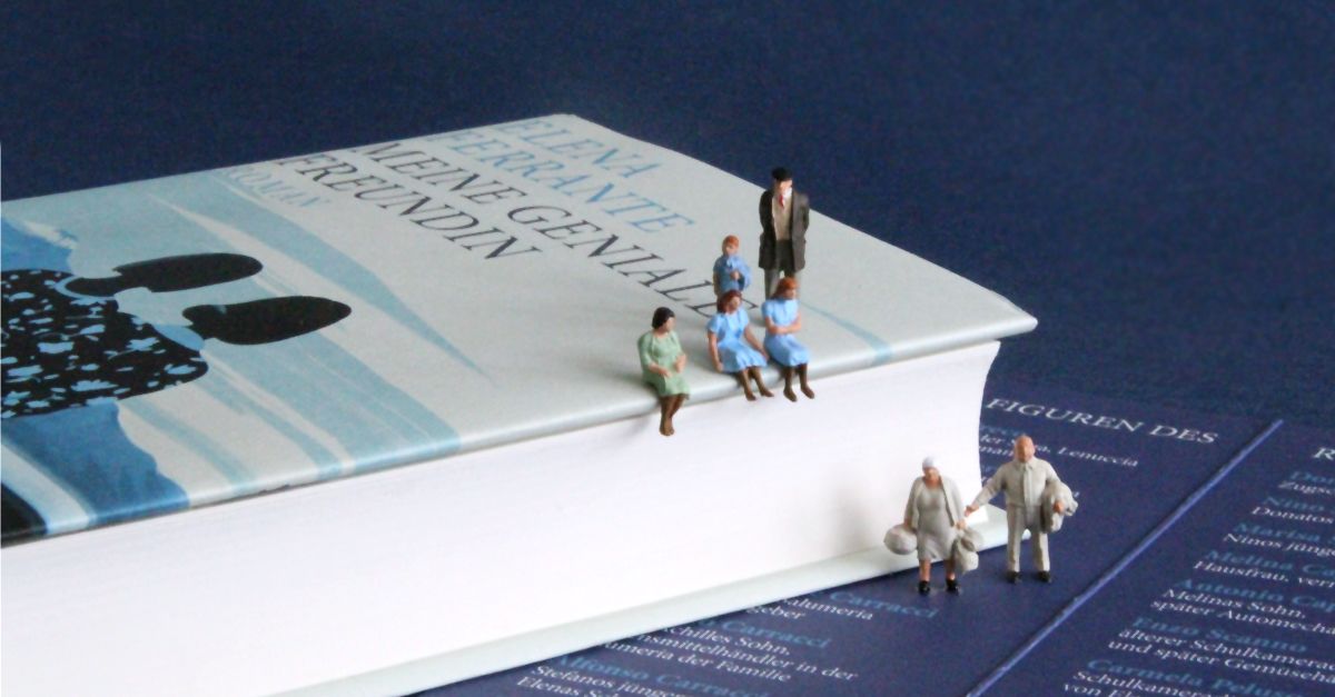 Seitenansicht des Buches »Meine Geniale Freundin«, auf dem fünf Miniaturfiguren sitzen. Zwei Figuren stehen vor dem Buch auf einem Lesezeichen.