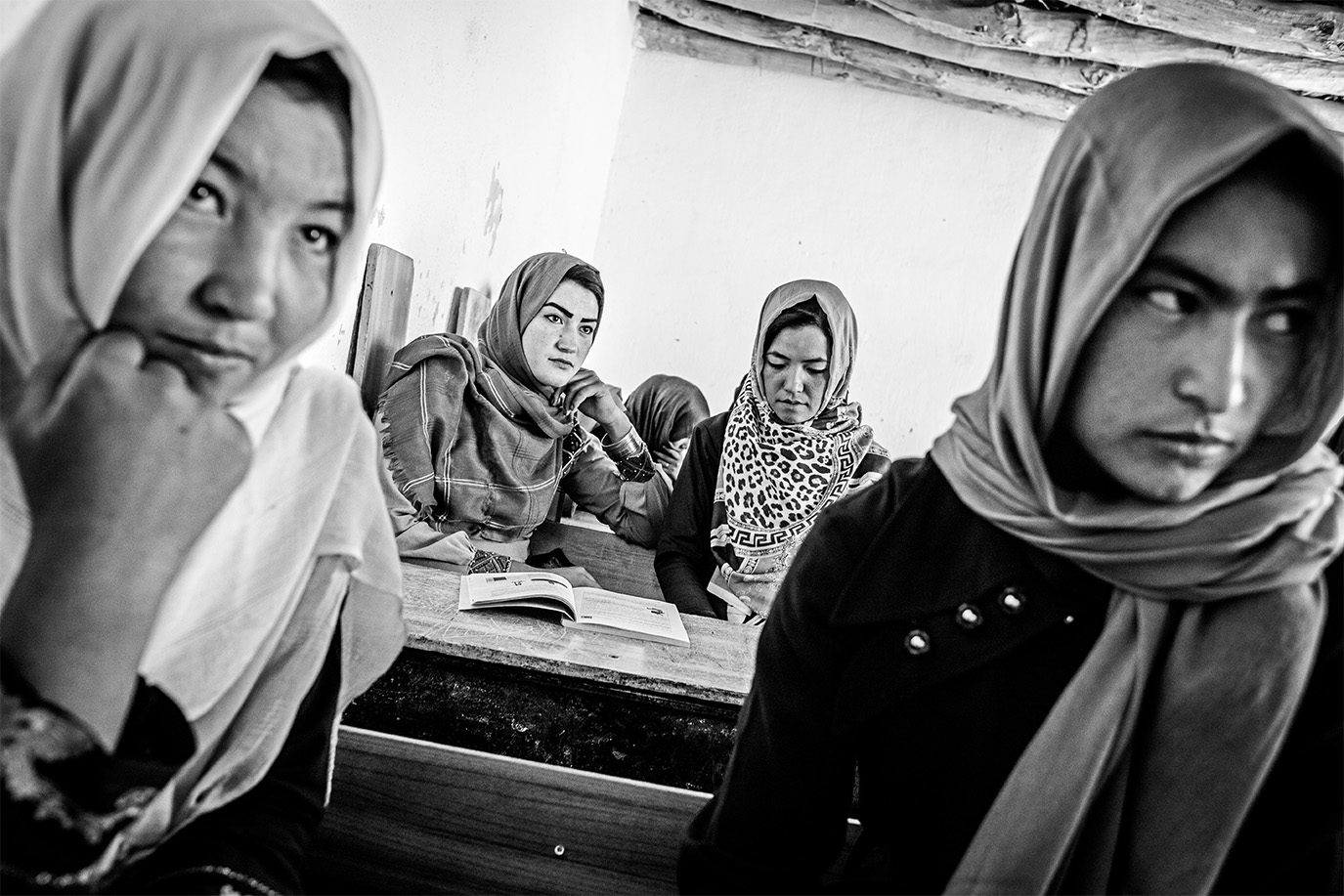 Eine schwarz-weiß Fotografie von afghanischen Frauen mit Kopftuch, die in einer Schule sitzen. © Andy Spyra